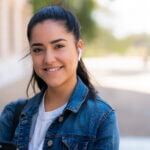 Portrait of young woman listening to music with earpods while standing outdoors on the street. Urban concept.